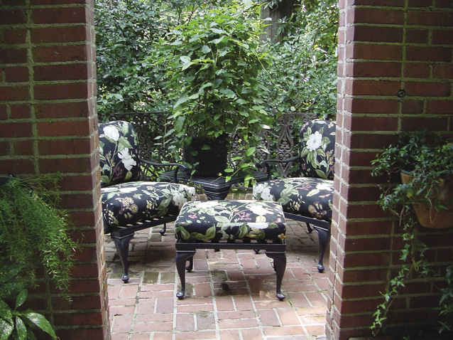 Floral patterned patio furniture on a small brick patio surrounded by green foliage.